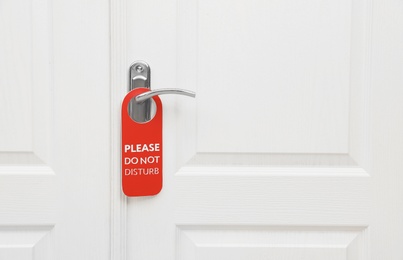 Closed door with sign PLEASE DO NOT DISTURB on handle at hotel, space for text