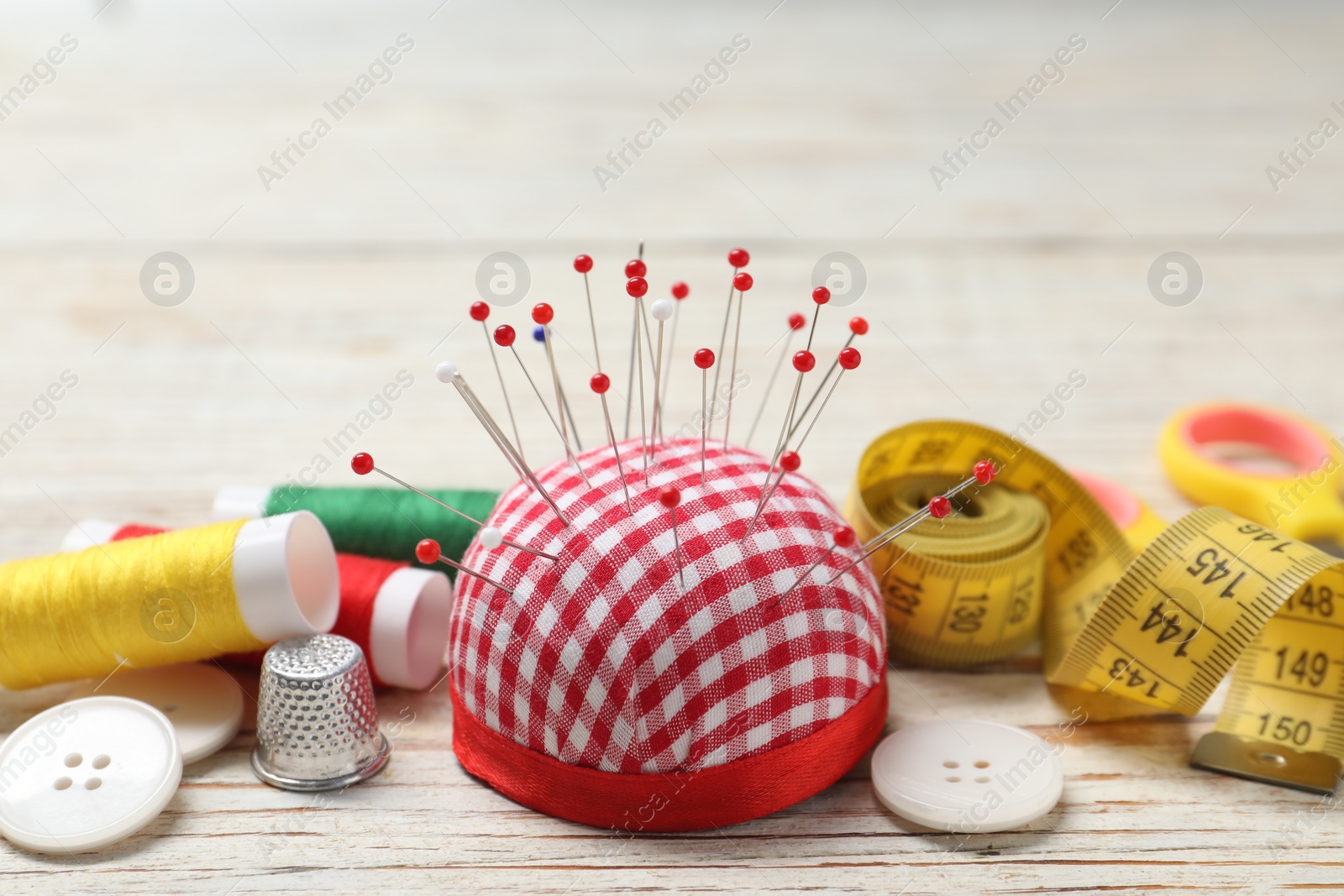 Photo of Checkered pincushion with pins and other sewing tools on light wooden table