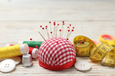 Photo of Checkered pincushion with pins and other sewing tools on light wooden table