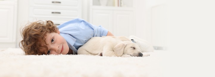 Image of Little boy lying with cute puppies on white carpet at home. Banner design with space for text