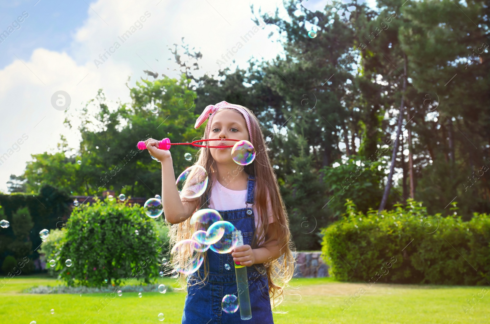 Photo of Cute little girl blowing soap bubbles in green park