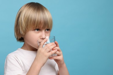 Cute little boy drinking fresh water from glass on light blue background, space for text