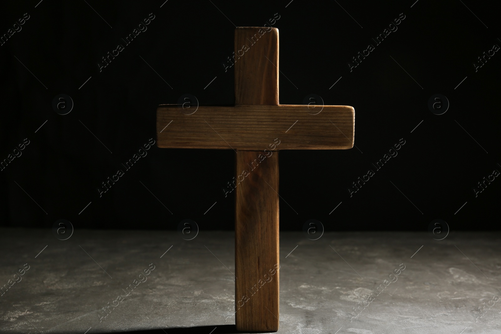 Photo of Wooden Christian cross on grey stone table against black background. Religion concept