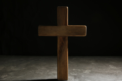 Wooden Christian cross on grey stone table against black background. Religion concept