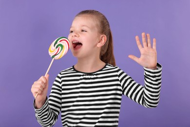 Photo of Happy little girl with colorful lollipop swirl on violet background