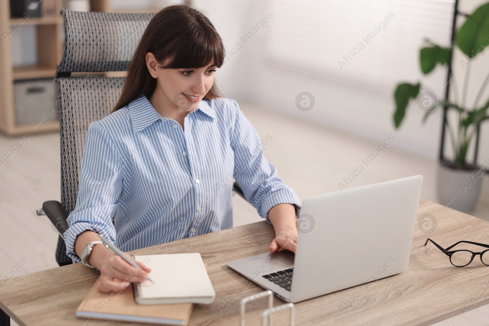 Photo of Woman taking notes during webinar at wooden table indoors