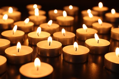 Photo of Burning tealight candles on dark surface, closeup