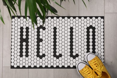 Photo of Stylish door mat with word Hello, shoes and houseplant on floor, flat lay