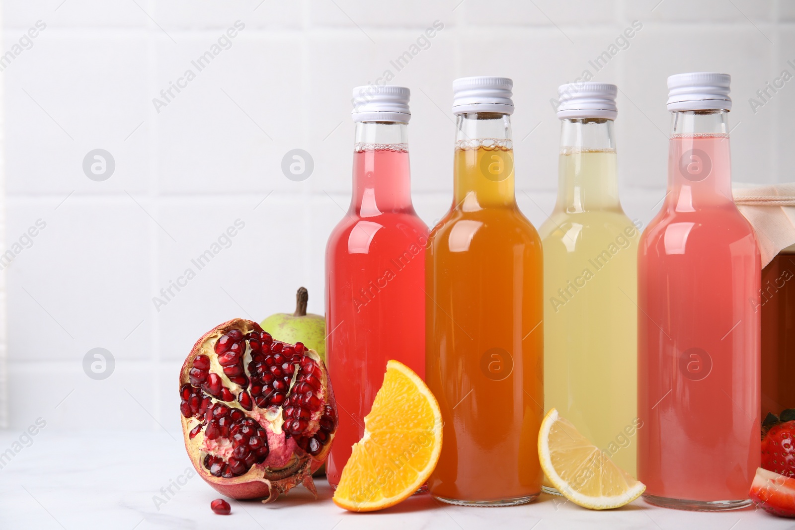 Photo of Delicious kombucha in glass bottles and fresh fruits on white marble table