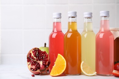 Delicious kombucha in glass bottles and fresh fruits on white marble table