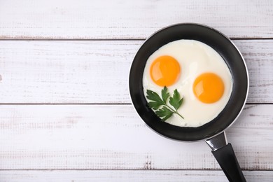 Tasty fried eggs with parsley in pan on white wooden table, top view. Space for text