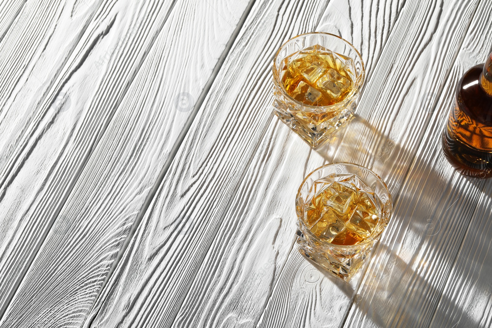 Photo of Whiskey with ice cubes in glasses on white wooden table, above view. Space for text