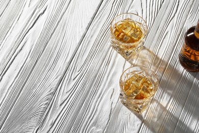 Photo of Whiskey with ice cubes in glasses on white wooden table, above view. Space for text