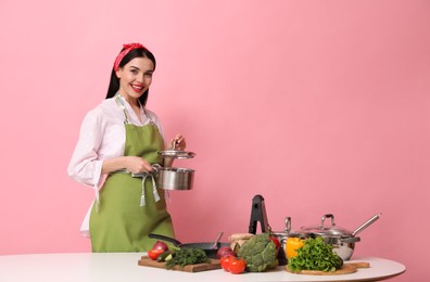 Photo of Young housewife with vegetables and different utensils on pink background. Space for text