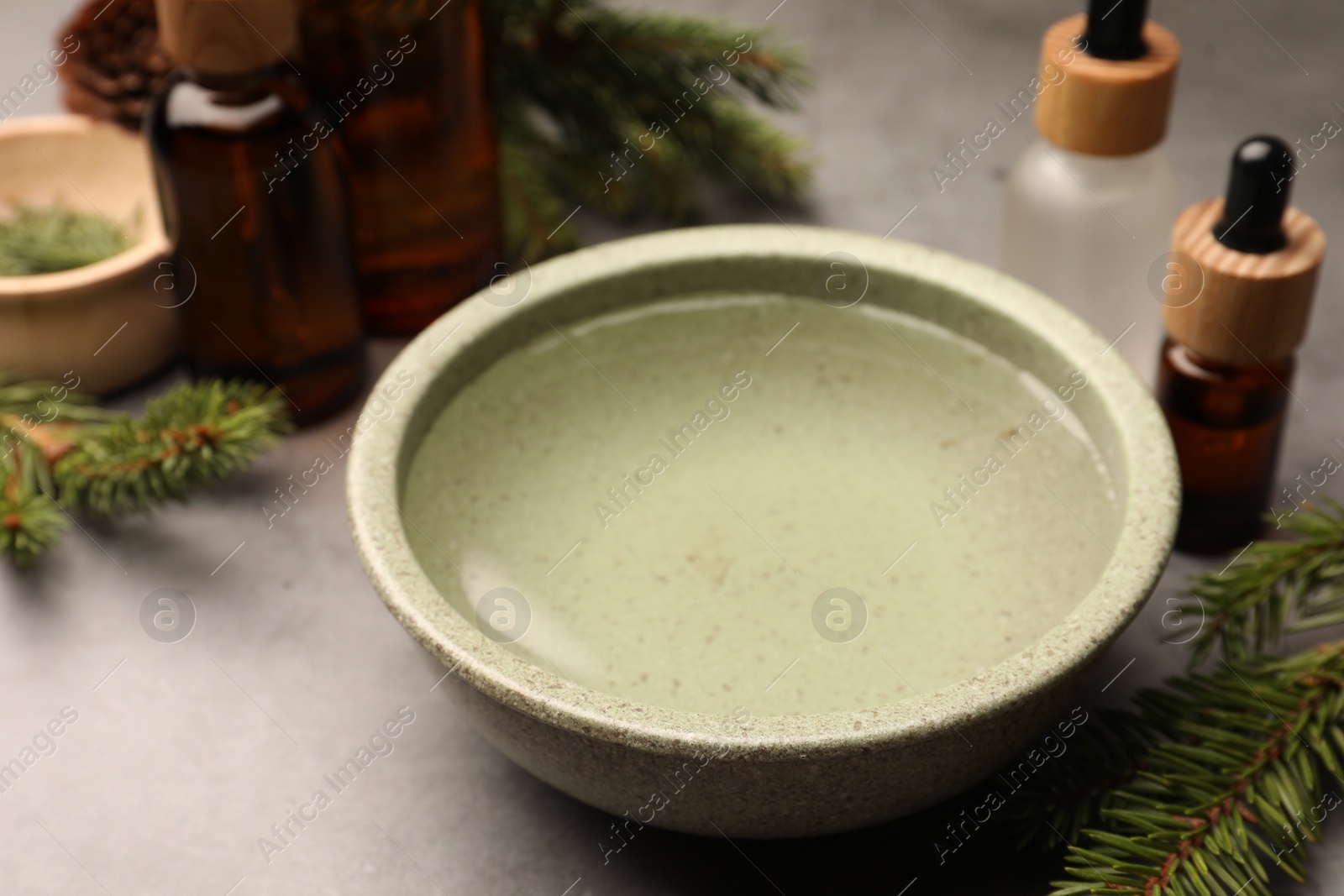 Photo of Bowl of essential oil and fir twigs on grey table, closeup. Aromatherapy treatment