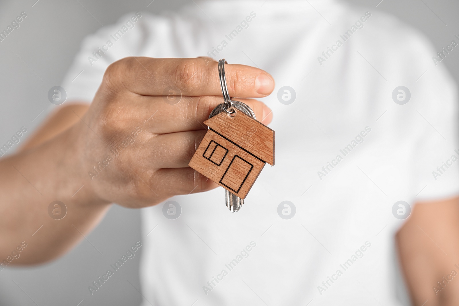 Photo of Young woman holding house key with trinket on grey background, closeup