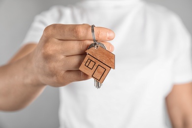 Photo of Young woman holding house key with trinket on grey background, closeup