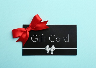 Photo of Gift card with bow on light blue background, top view