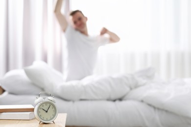 Photo of Man stretching on bed at home in morning, focus on alarm clock. Space for text
