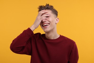 Photo of Young man covering eyes with hand and laughing on orange background