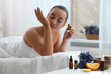 Photo of Young woman with bottle of essential oil in spa salon