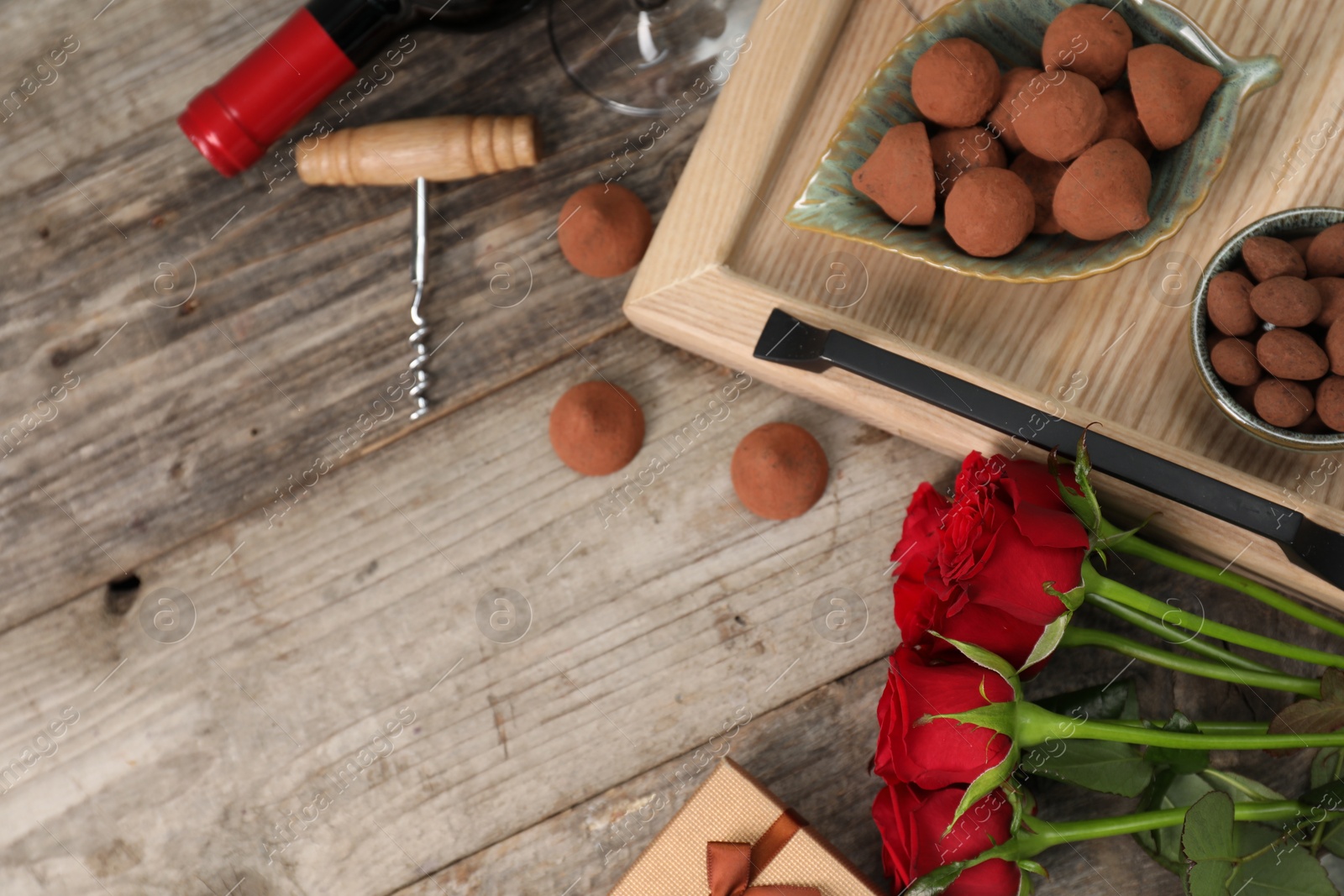 Photo of Red wine, chocolate truffles, corkscrew and roses on wooden table, above view. Space for text