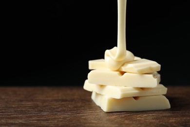 Photo of Pouring tasty white chocolate paste onto pieces on wooden table, closeup. Space for text