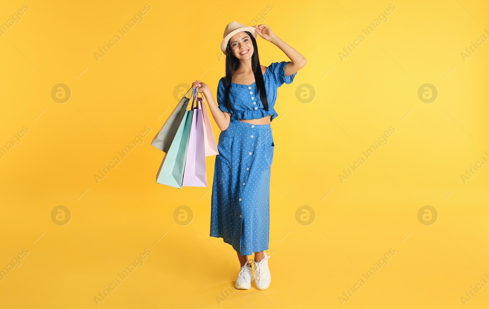 Photo of Beautiful young woman with paper shopping bags on yellow background