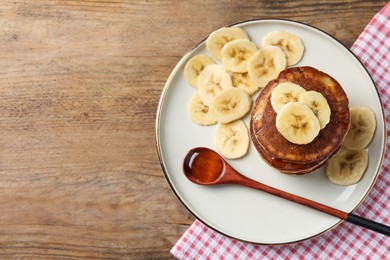 Photo of Plate of banana pancakes with honey on wooden table, top view. Space for text