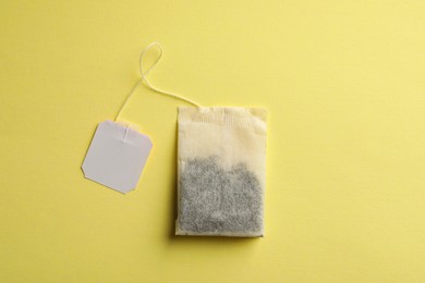 Photo of Paper tea bag with tag on yellow background, top view