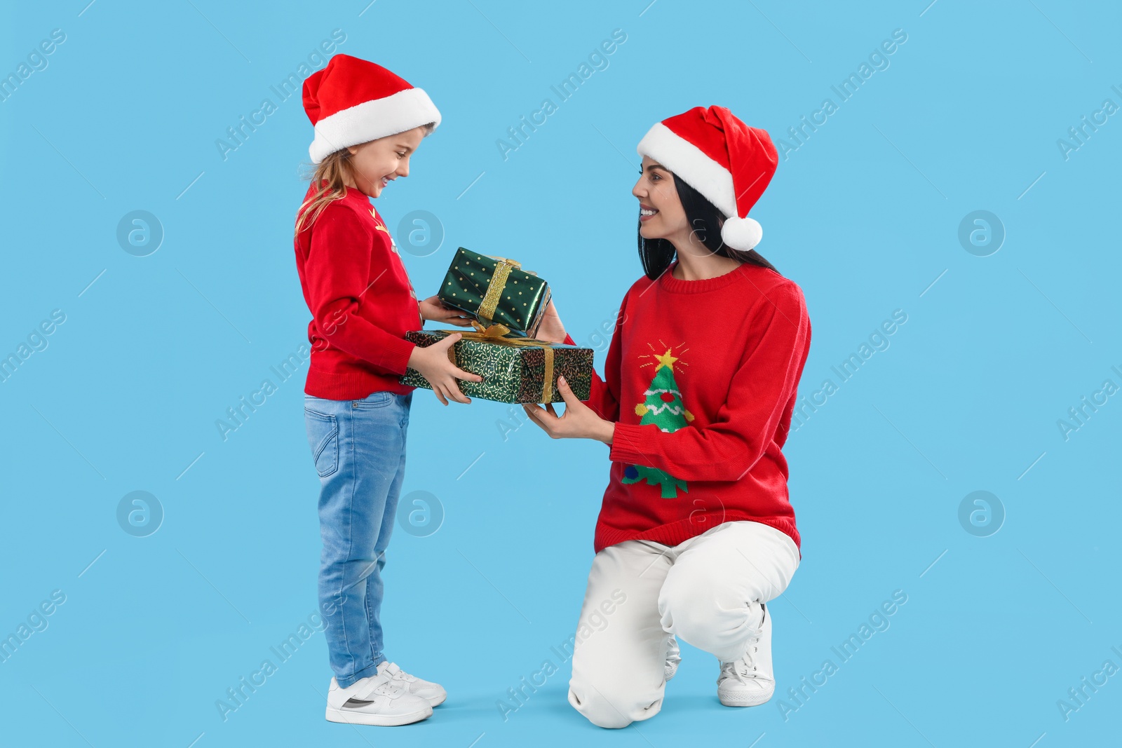 Photo of Mother and daughter exchanging Christmas gifts on light blue background