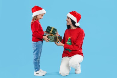 Photo of Mother and daughter exchanging Christmas gifts on light blue background