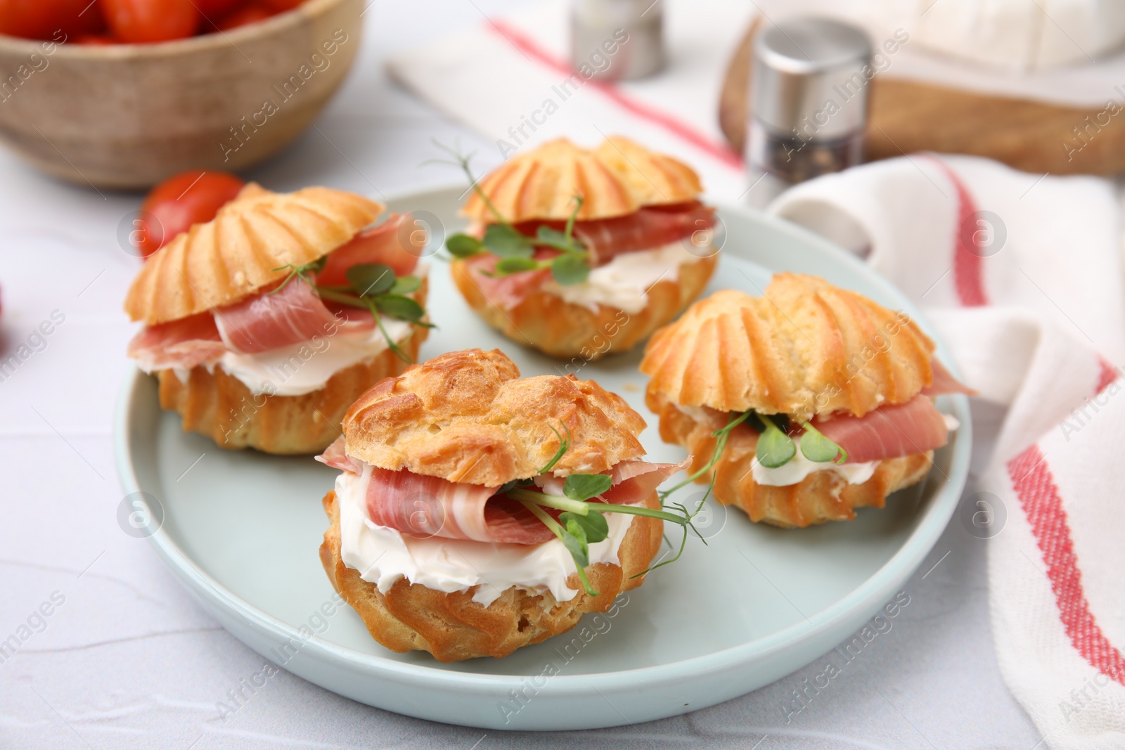 Photo of Delicious profiteroles with cream cheese and prosciutto on white table, closeup