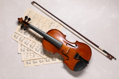 Photo of Violin, bow and music sheets on grey marble table, top view