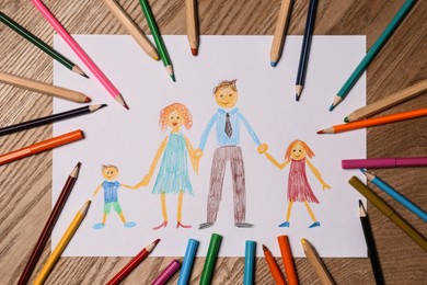 Photo of Family drawing and colorful pencils on wooden table, flat lay