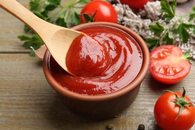 Photo of Bowl and spoon with tasty ketchup, fresh tomatoes, parsley and spices on wooden table