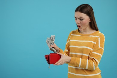 Woman putting money into wallet on light blue background, space for text