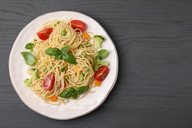 Delicious pasta primavera with tomatoes, basil and broccoli on grey table, top view. Space for text