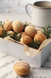 Homemade walnut shaped cookies and fir branches in box on white wooden table, closeup. Bokeh effect