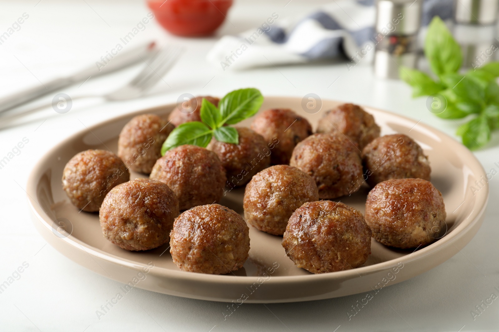Photo of Tasty cooked meatballs with basil on white table, closeup