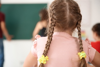 Photo of Cute little child with adorable braids in classroom. Elementary school