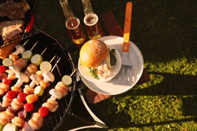 Tasty burger on table near barbecue grill outdoors, flat lay