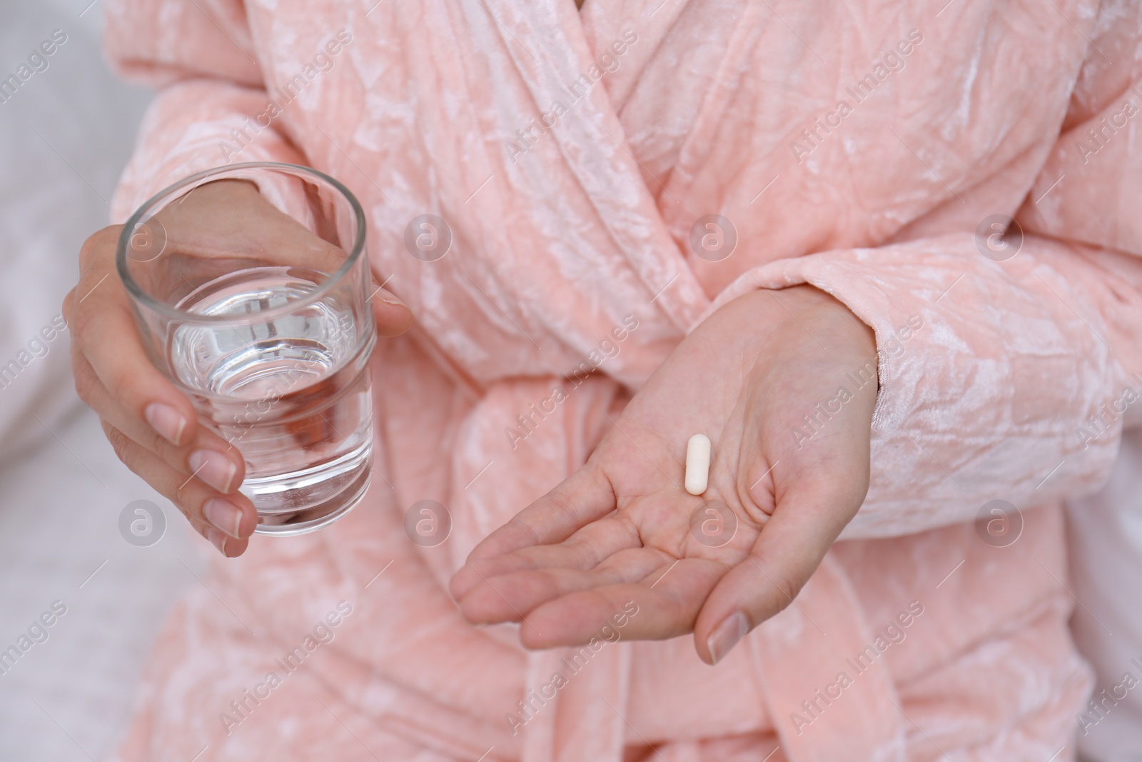 Photo of Woman holding glass of water and pill in bedroom, closeup