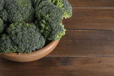 Photo of Bowl with fresh raw broccoli on wooden table, above view and space for text