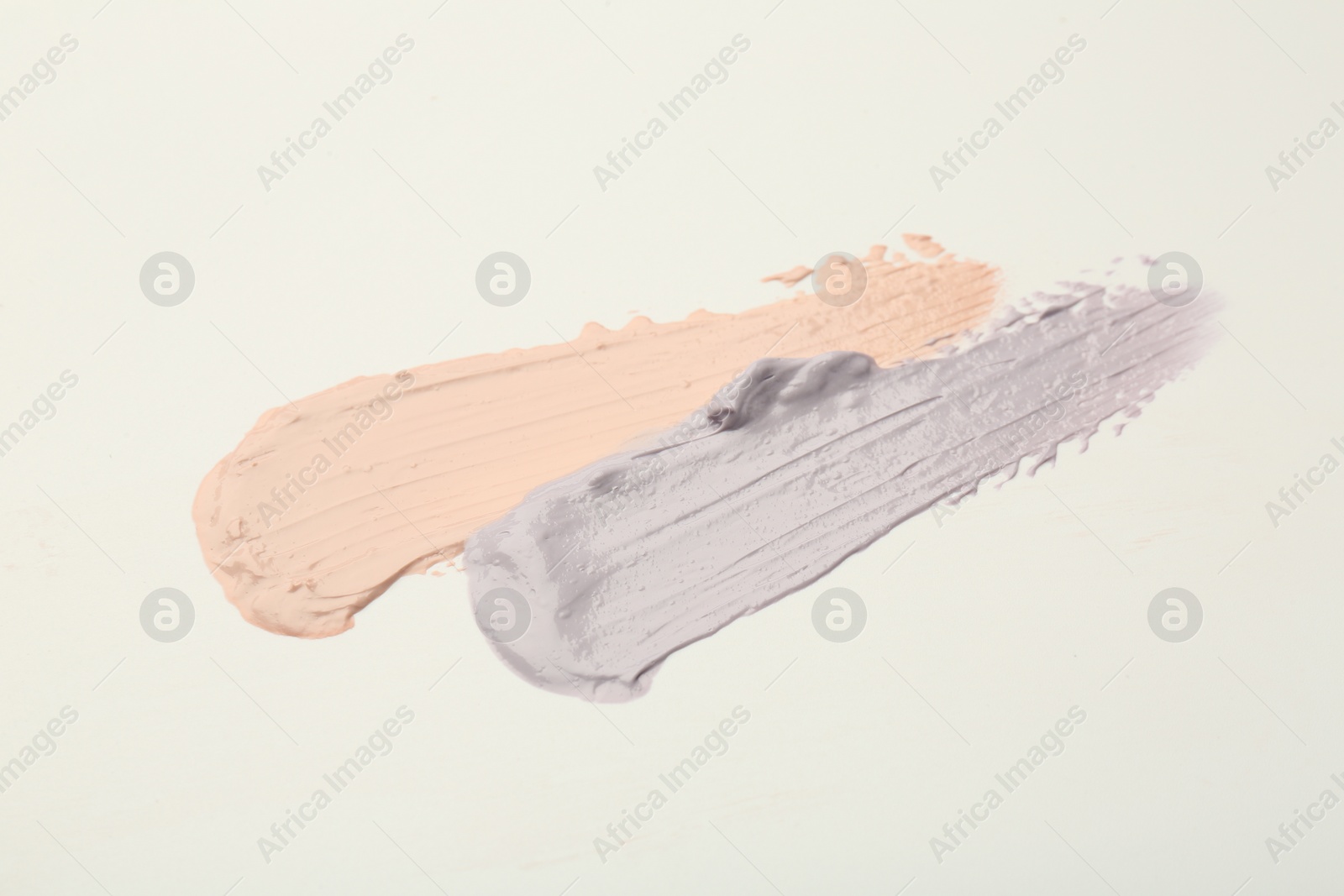 Photo of Strokes of pink and purple color correcting concealers on white background