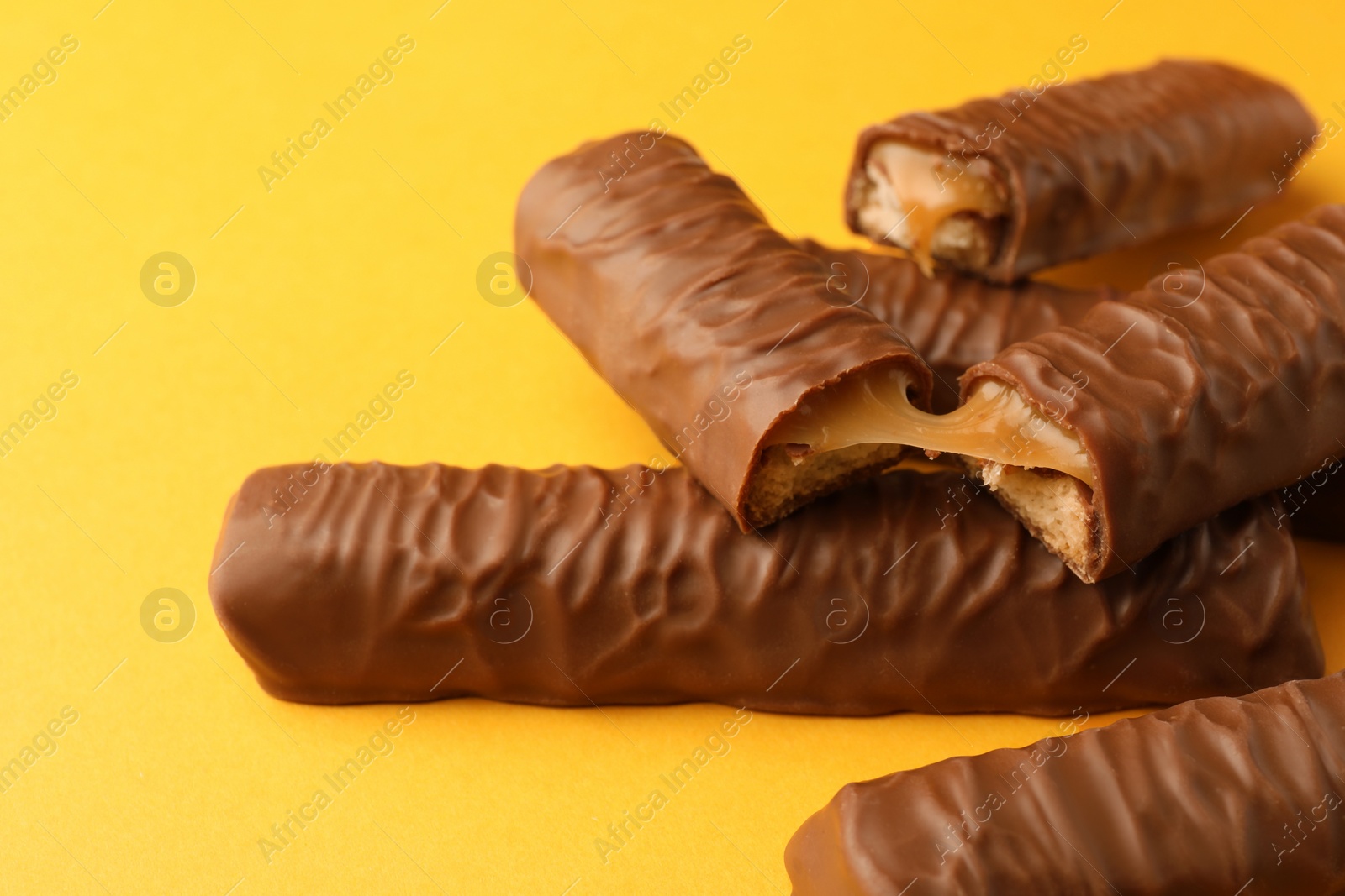 Photo of Sweet tasty chocolate bars with caramel on yellow background, closeup