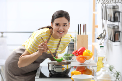 Young woman cooking tasty soup in kitchen