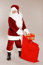 Photo of Authentic Santa Claus with sack and gift on grey background