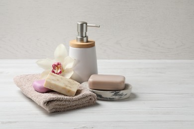 Photo of Soap bars, liquid dispenser and terry towel on white wooden table. Space for text