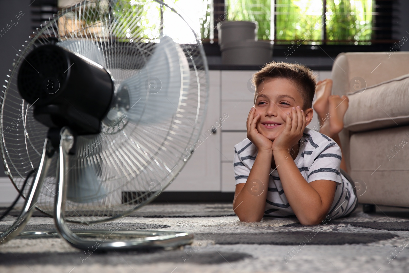 Photo of Little boy enjoying air flow from fan at home. Summer heat